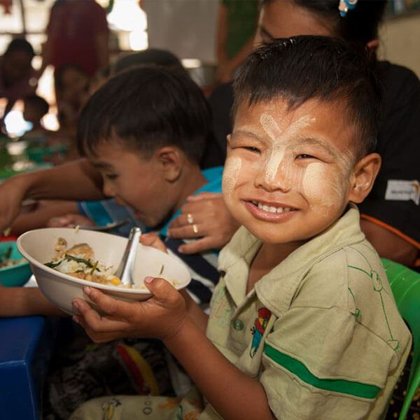 一名透過世界宣明會接受助養的男童，捧著一碗食物咧嘴而笑。