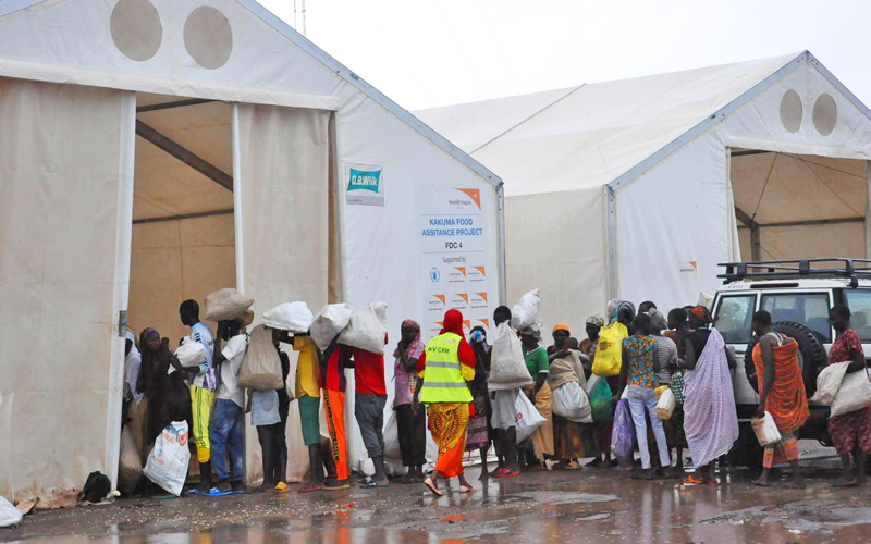 a crowd of people holding white sacks, lined up in front of two large white tents and a white SUV